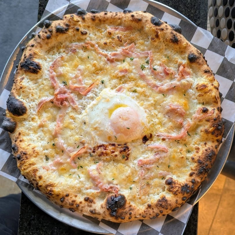 Pop-Start Pizza's white pizza with ham, cheese, and a fried egg on a checkered paper.