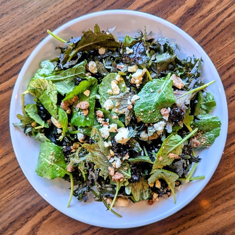 Overhead view of a fresh green salad with feta cheese and nuts in a white bowl.