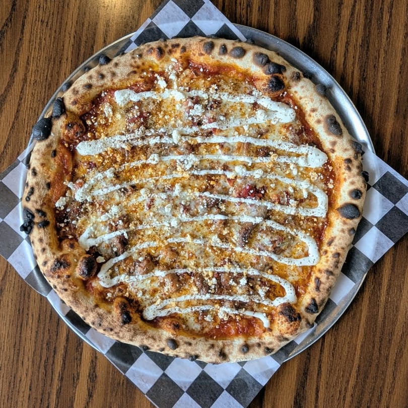 A Pop-Start Pizza with white sauce drizzled over cheese and a crispy crust on a checkered paper.