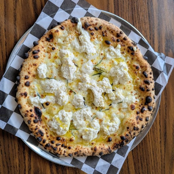 A white pizza from Pop-Start Pizza, topped with ricotta cheese, olive oil, and herbs.